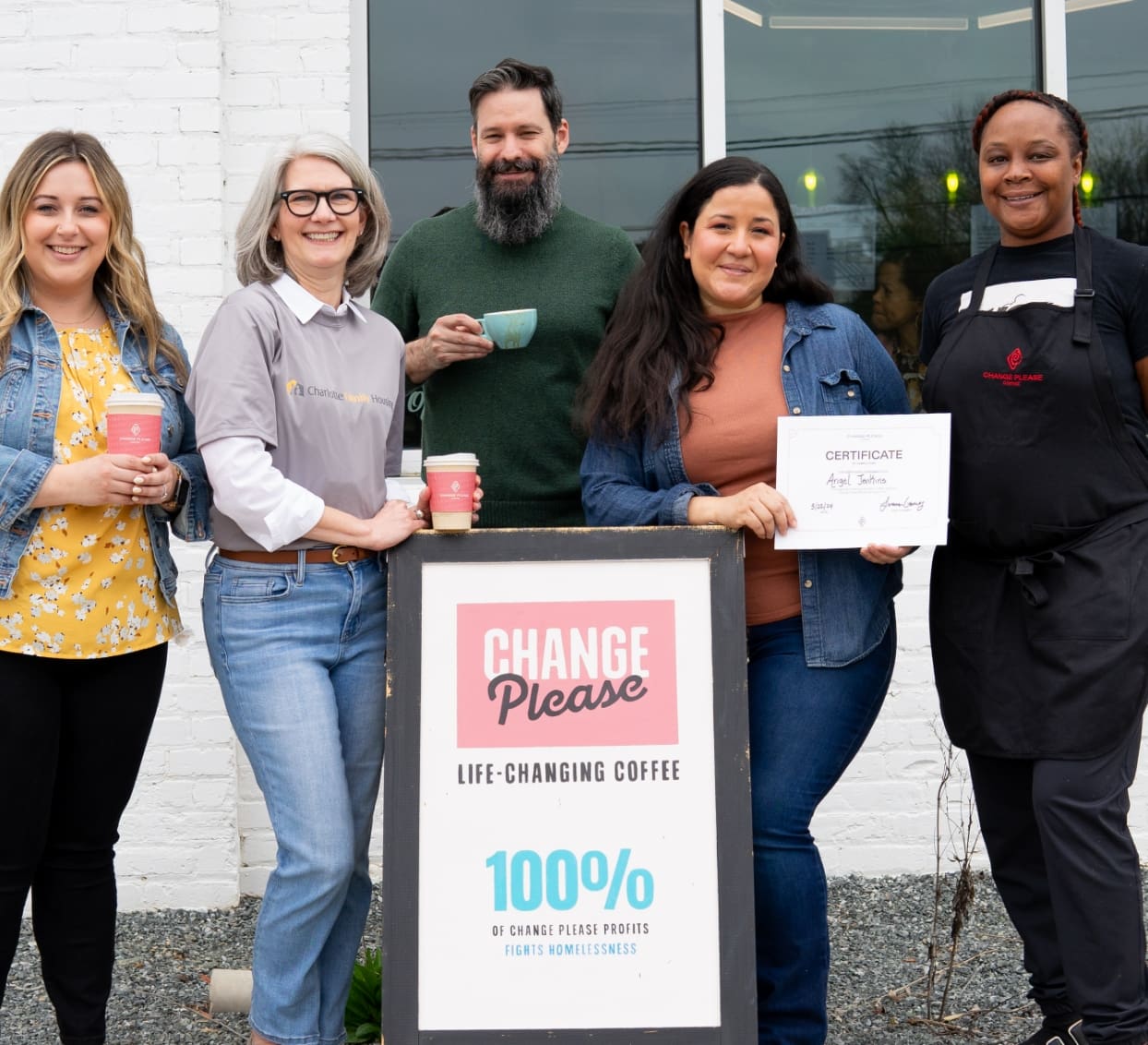 Group holding coffee and certificate outside café