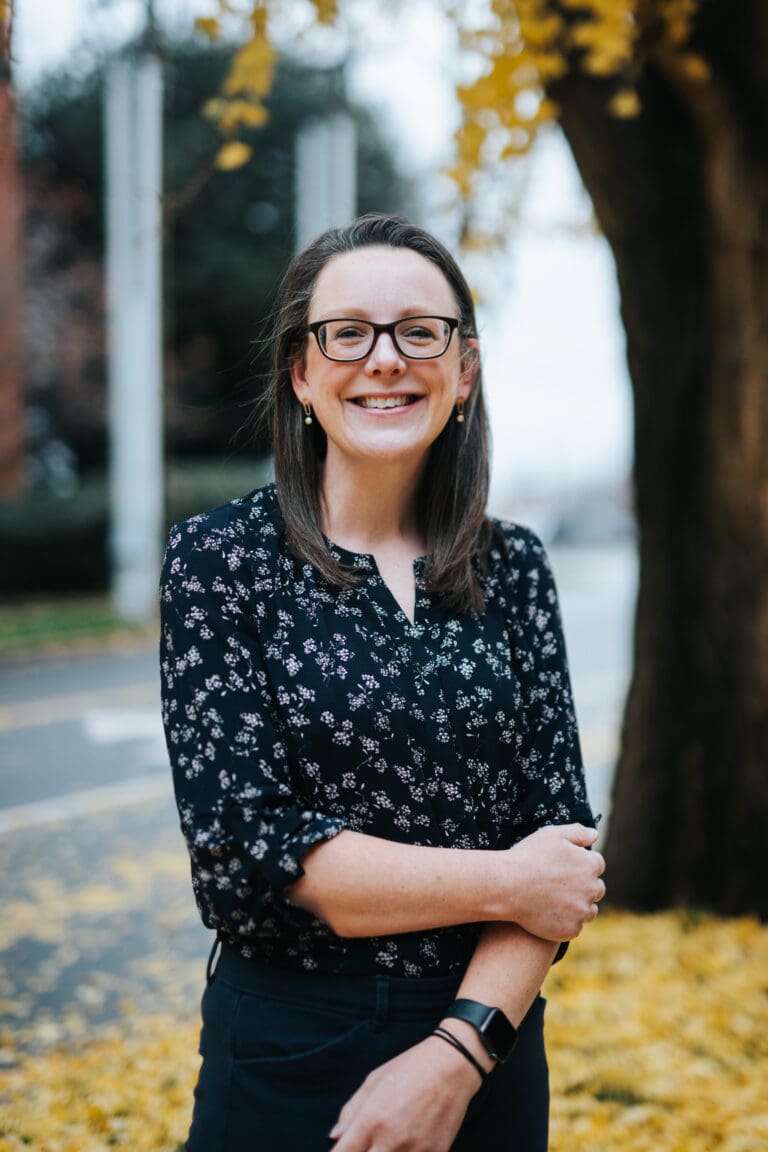 Smiling person outdoors with fall leaves background.