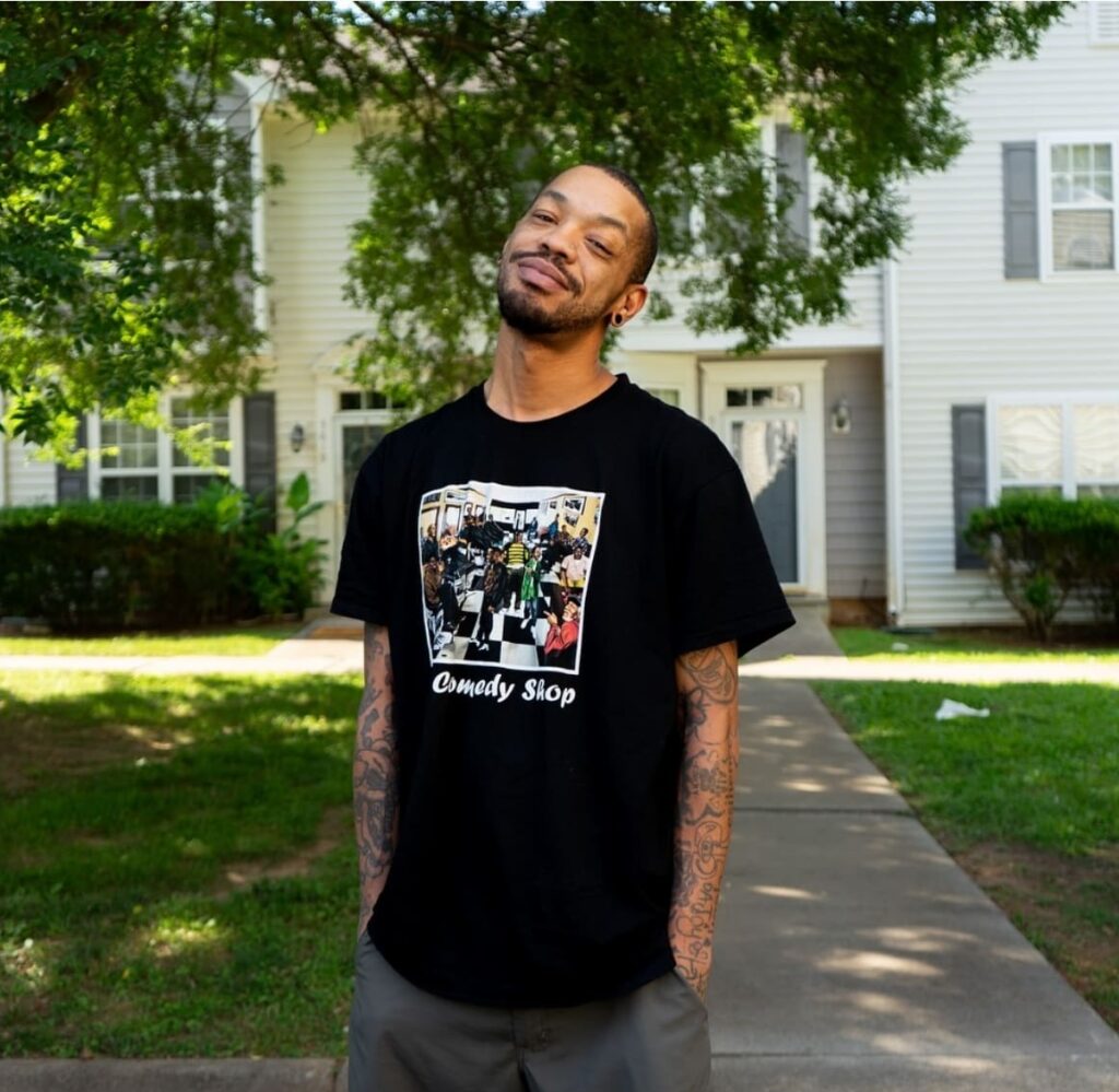 Smiling man in Comedy Shop t-shirt outside house