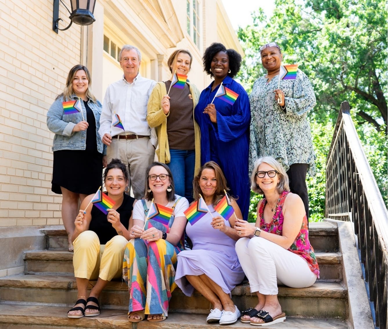 CFH Staff holding rainbow flags on steps outdoors.