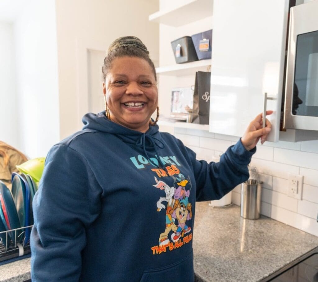 Smiling woman in kitchen, wearing cartoon hoodie.